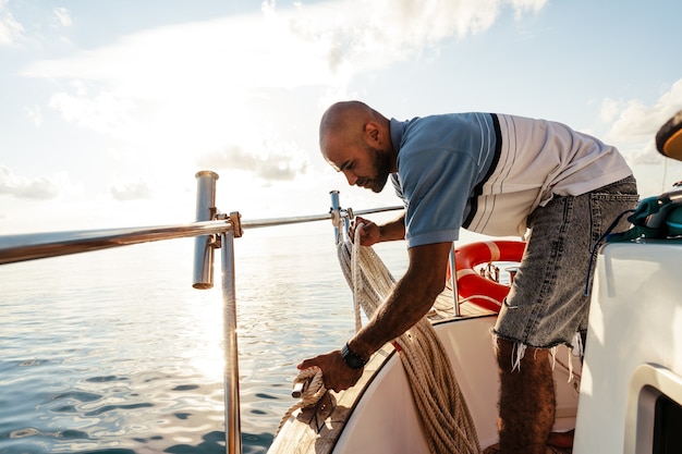 Giovane marinaio afroamericano che lega le corde sulla barca a vela nel mare al tramonto, primo piano