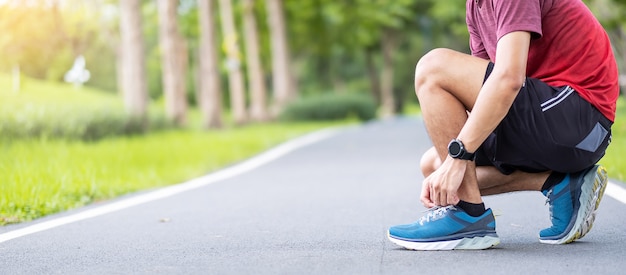 Giovane maschio adulto in abiti sportivi e smartwatch legare i lacci delle scarpe nel parco