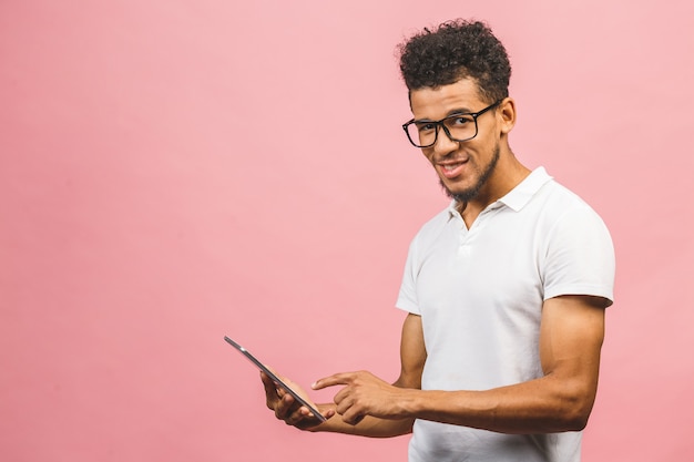 Giovane maschio afroamericano di risata che giudica un PC della compressa del cuscinetto di tocco isolato contro fondo rosa