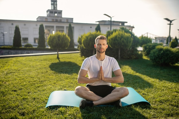 Giovane maschio barbuto a praticare yoga all'esterno, mani in namaste