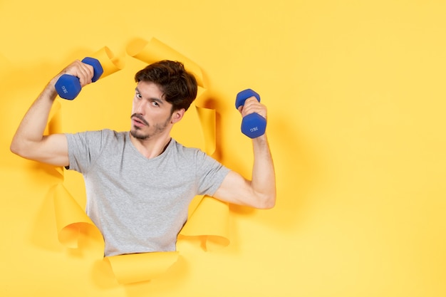 giovane maschio che si allena con manubri blu su sfondo giallo esercizio atleta sport gym