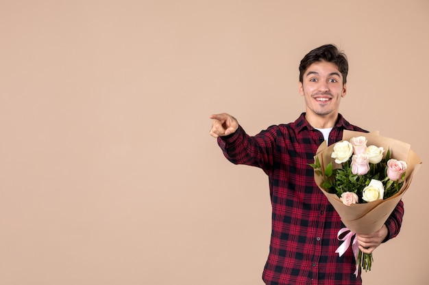 Giovane maschio di vista frontale che tiene bei fiori sulla parete marrone