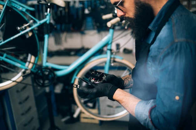 Giovane meccanico della bicicletta della barba che ripara le biciclette in un'officina.