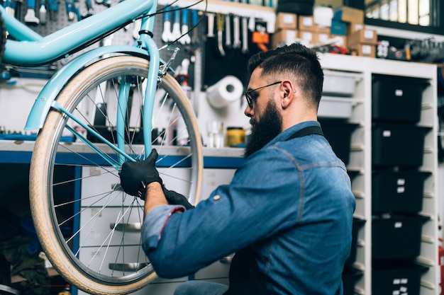 Giovane meccanico della bicicletta della barba che ripara le biciclette in un'officina.