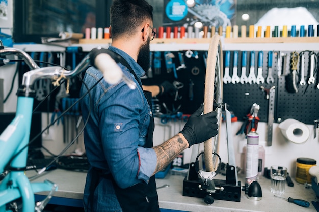 Giovane meccanico della bicicletta della barba che ripara le biciclette in un'officina.