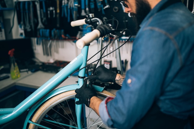 Giovane meccanico della bicicletta della barba che ripara le biciclette in un'officina.