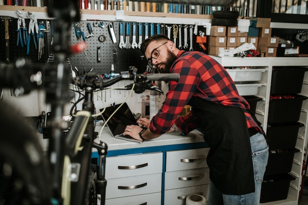 Giovane meccanico della bicicletta della barba che ripara le biciclette in un'officina.