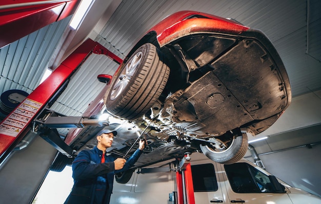 Giovane meccanico di auto presso la stazione di servizio di riparazione che ispeziona la ruota dell'auto