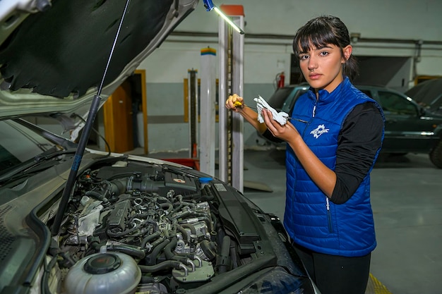 Giovane meccanico femminile che controlla i livelli dell'olio di un motore di automobile