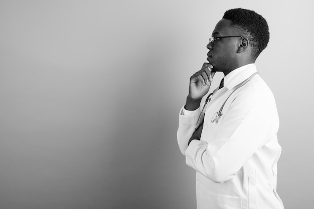 giovane medico africano che indossa occhiali da vista contro il muro bianco. bianco e nero