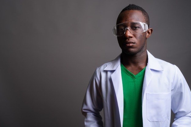 Giovane medico africano dell'uomo che indossa gli occhiali protettivi sulla parete grigia