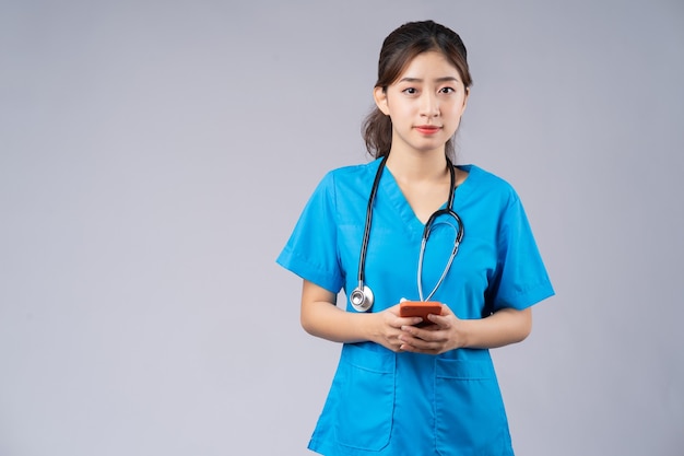 Giovane medico asiatico con lo smartphone su grigio