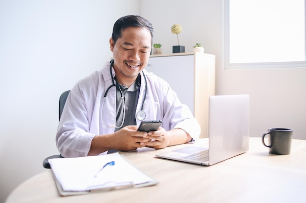 Giovane medico asiatico felice che tiene lo smartphone pronto per la consultazione online di telemedicina in ambito medico