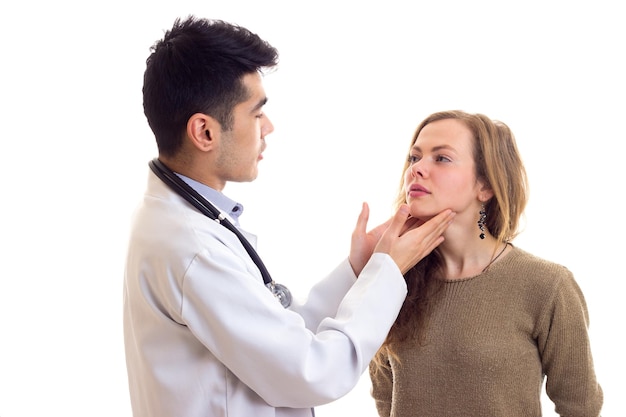 Giovane medico bello con i capelli scuri in abito bianco con lo stetoscopio sul collo che esamina la giovane donna