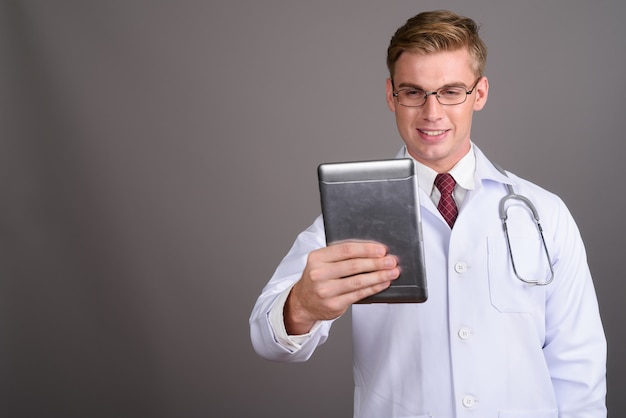 Giovane medico bello dell'uomo con capelli biondi sulla parete grigia