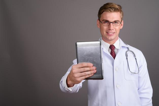 Giovane medico bello dell'uomo con capelli biondi sulla parete grigia