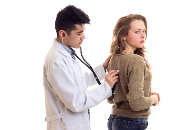 Giovane medico bello in abito bianco con lo stetoscopio che ascolta la parte posteriore della giovane donna affascinante