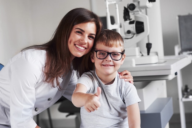 Giovane medico biondo femminile attraente che sorride con il suo piccolo paziente soddisfatto. Gli occhiali sono perfettamente selezionati.