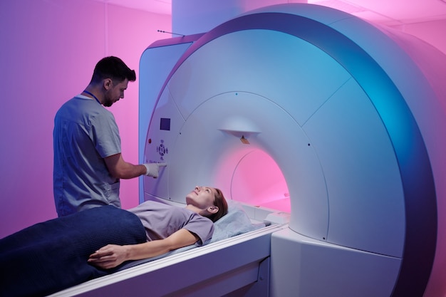 Giovane medico che preme il pulsante sul pannello per avviare la procedura di scansione mri