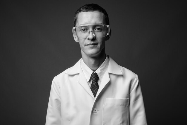 giovane medico come scienziato che indossa occhiali protettivi contro il muro grigio in bianco e nero