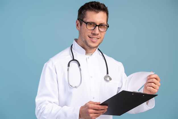 Giovane medico con gli occhiali camice bianco e stetoscopio che tiene la cartella con un rapporto in mano Concetto di medicina