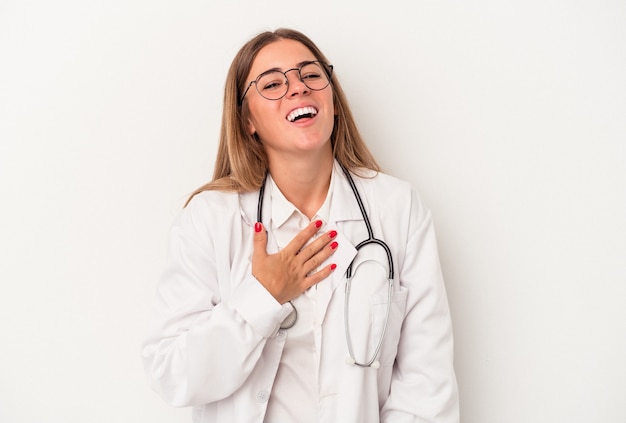 Giovane medico donna russa isolata su sfondo bianco ride ad alta voce tenendo la mano sul petto.