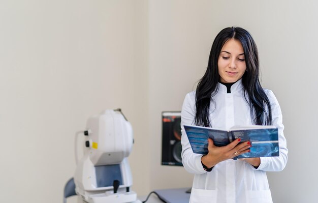 Giovane medico femminile che sorride felicemente in posa in ufficio vicino alla macchina per la scansione. Tecnologia dell'industria medica. Attrezzature moderne in clinica.