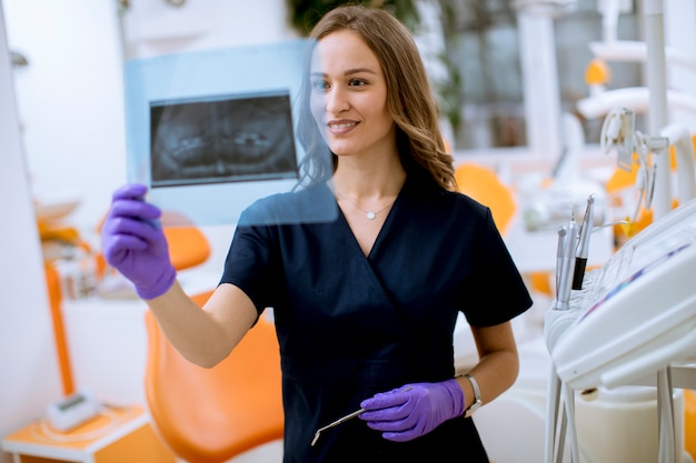 Giovane medico femminile con i guanti protettivi che esaminano radiografia nell'ufficio del dentista