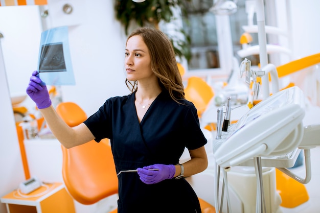 Giovane medico femminile con i guanti protettivi che esaminano radiografia nell'ufficio del dentista