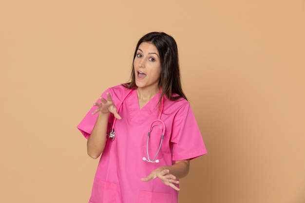 Giovane medico femminile con un'uniforme rosa che gesturing sopra la parete marrone