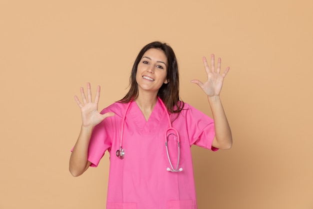 Giovane medico femminile con un'uniforme rosa che gesturing sopra la parete marrone