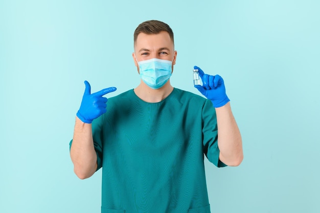 Giovane medico in maschera medica e camice bianco con stetoscopio che tiene la siringa isolata sul blu