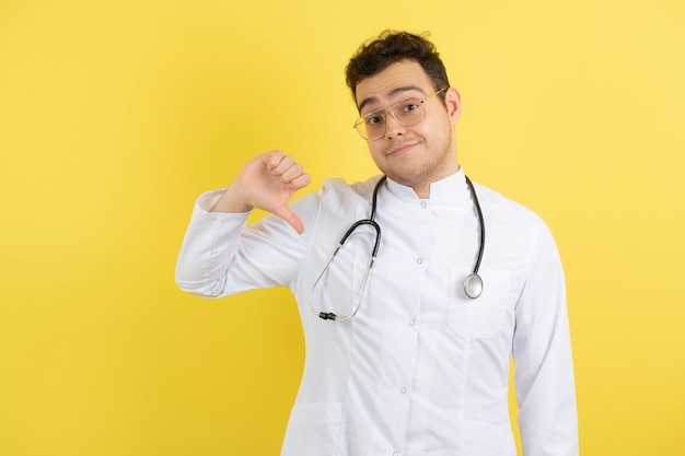 Giovane medico maschio in camice bianco in piedi e dando i pollici verso il basso.