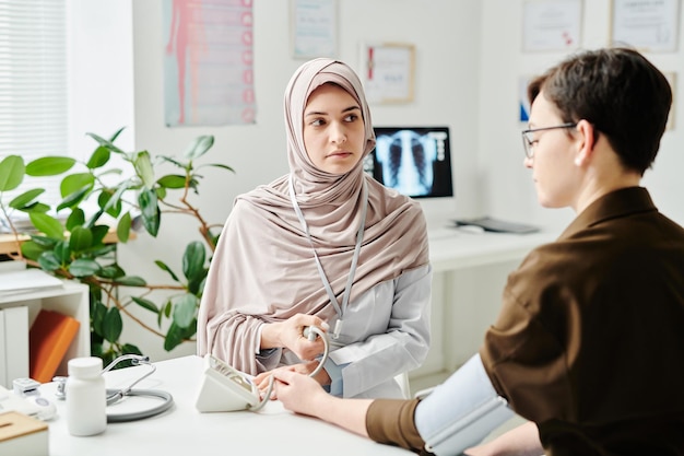 Giovane medico musulmano serio che misura la pressione del paziente femminile malato