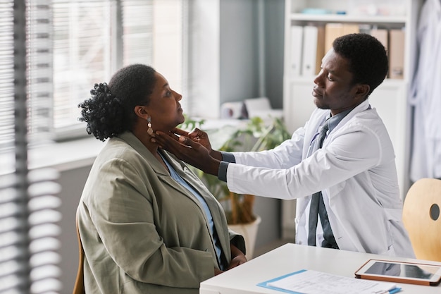 Giovane medico nero che palpa la donna d'esame del collo in clinica