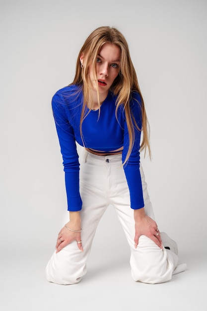Giovane modella in top blu e pantaloni bianchi che posa su sfondo bianco