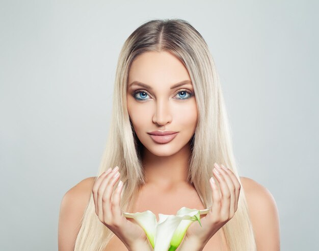 Giovane modello femminile perfetto donna con pelle fresca pulita capelli biondi sani e fiori di giglio nelle sue mani trattamento viso cosmetologia bellezza cura della pelle e spa