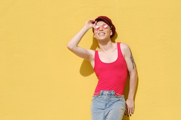 Giovane modello non binario che sorride mentre posa all'aperto appoggiato a un muro giallo. Concetto di uguaglianza, diversità e genere non binario.