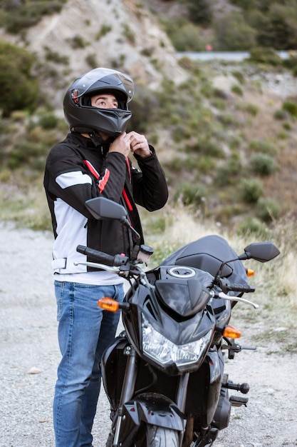 Giovane motociclista maschio che indossa il casco per guidare la sua moto