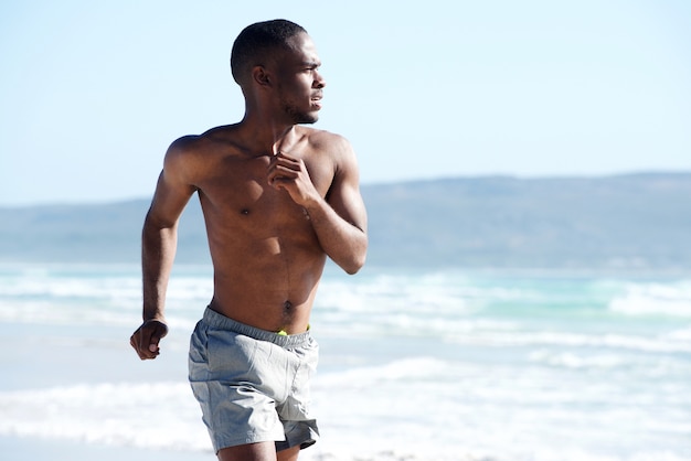 Giovane muscolare che corre lungo la spiaggia