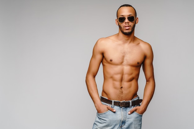 giovane muscoloso uomo afroamericano a torso nudo indossando occhiali da sole sul muro grigio chiaro