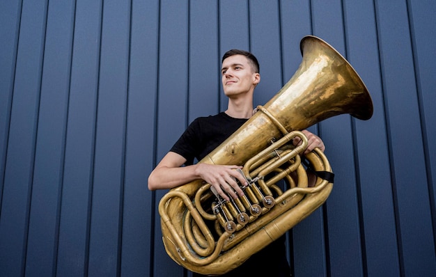 Giovane musicista di strada che suona la tuba vicino al grande muro blu