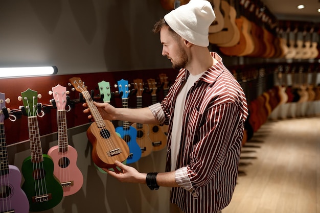 Giovane musicista uomo hipster che compra chitarra ukulele al negozio di strumenti musicali. Concetto di hobby, affari e commercio