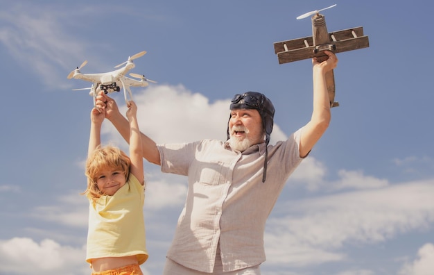 Giovane nipote e vecchio nonno che giocano con l'aereo giocattolo e il drone quadricottero contro il bambino del cielo pil