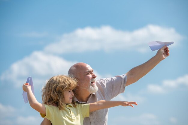 Giovane nipote e vecchio nonno con aeroplano di carta sopra il cielo blu e nuvole uomini generazione nonno