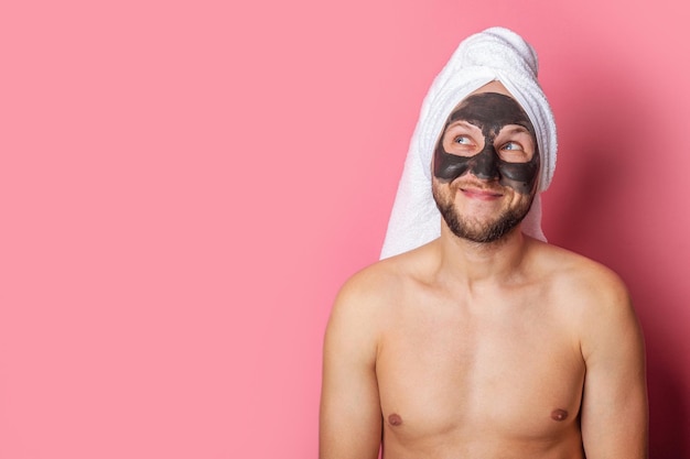 Giovane nudo sorridente con maschera cosmetica sul viso che guarda verso l'alto su sfondo rosa