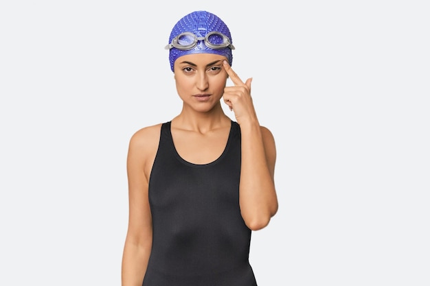 Giovane nuotatrice professionista caucasica che indica il tempio con il dito che pensa concentrato su un compito