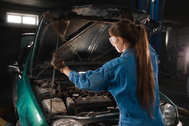 Giovane operaia addetta alle riparazioni auto Una meccanica donna controlla il livello dell'olio nel motore dell'auto Un meccanico controlla e mantiene un motore o un veicolo di un'auto da solo