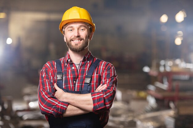 Giovane operaio allegro della grande fabbrica che ti guarda dentro l'officina