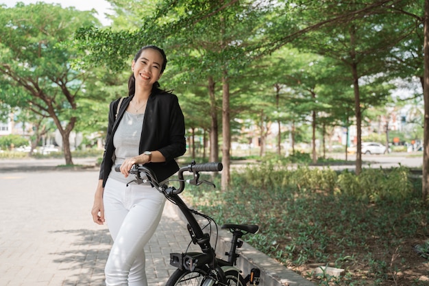 Giovane operaio asiatico sorridente della donna che sta con la sua bici pieghevole